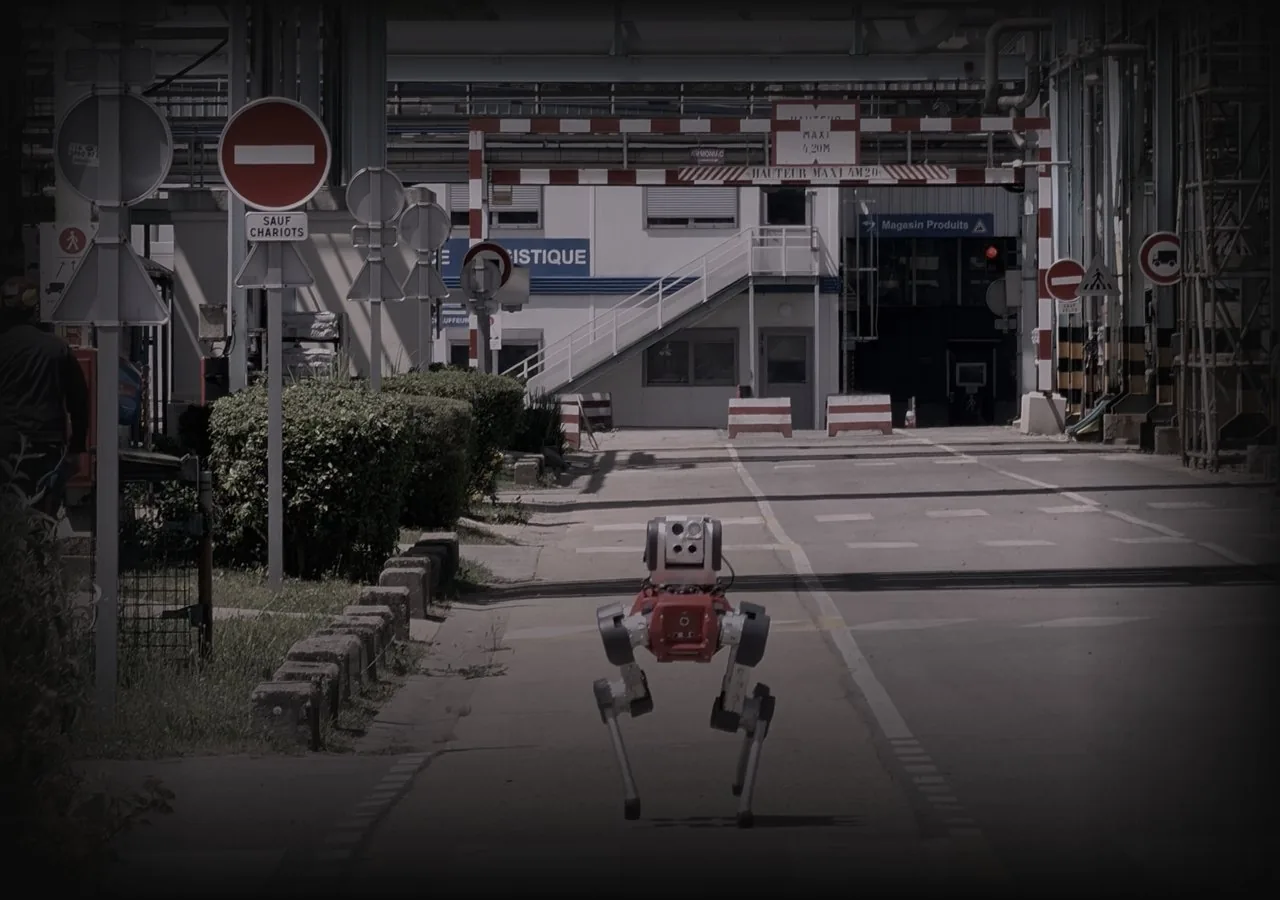 Robot d'inspection quadrupede en ronde autonome sur une voie d'usine, sous des racks de tuyauterie.