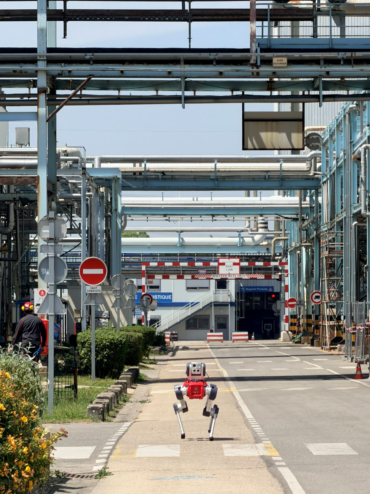 Un robot quadrupède d'inspection en ronde autonome dans une installation industrielle, entre les lignes de tuyauterie.